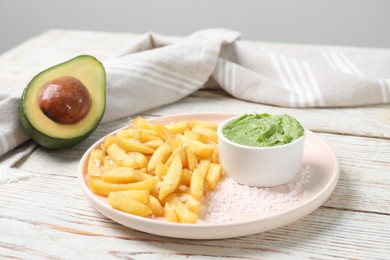 Plate with french fries, avocado and guacamole dip on white wooden table