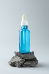 Photo of Bottle of cosmetic serum on stones against light grey background