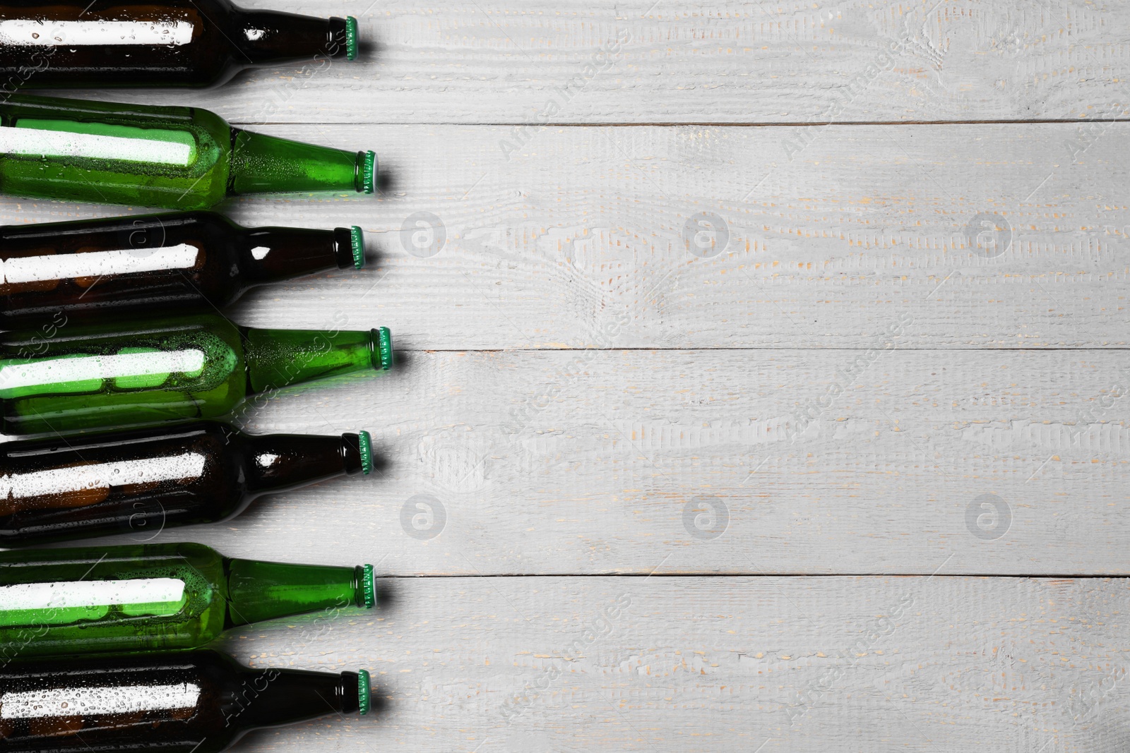 Photo of Glass bottles of beer on grey wooden background, flat lay. Space for text