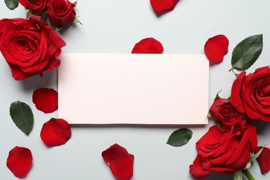 Blank card, beautiful red roses and petals on light background, flat lay. Space for text