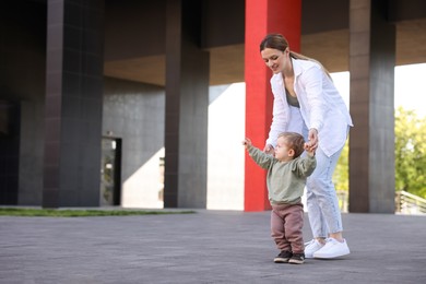 Happy nanny walking with cute little boy outdoors, space for text