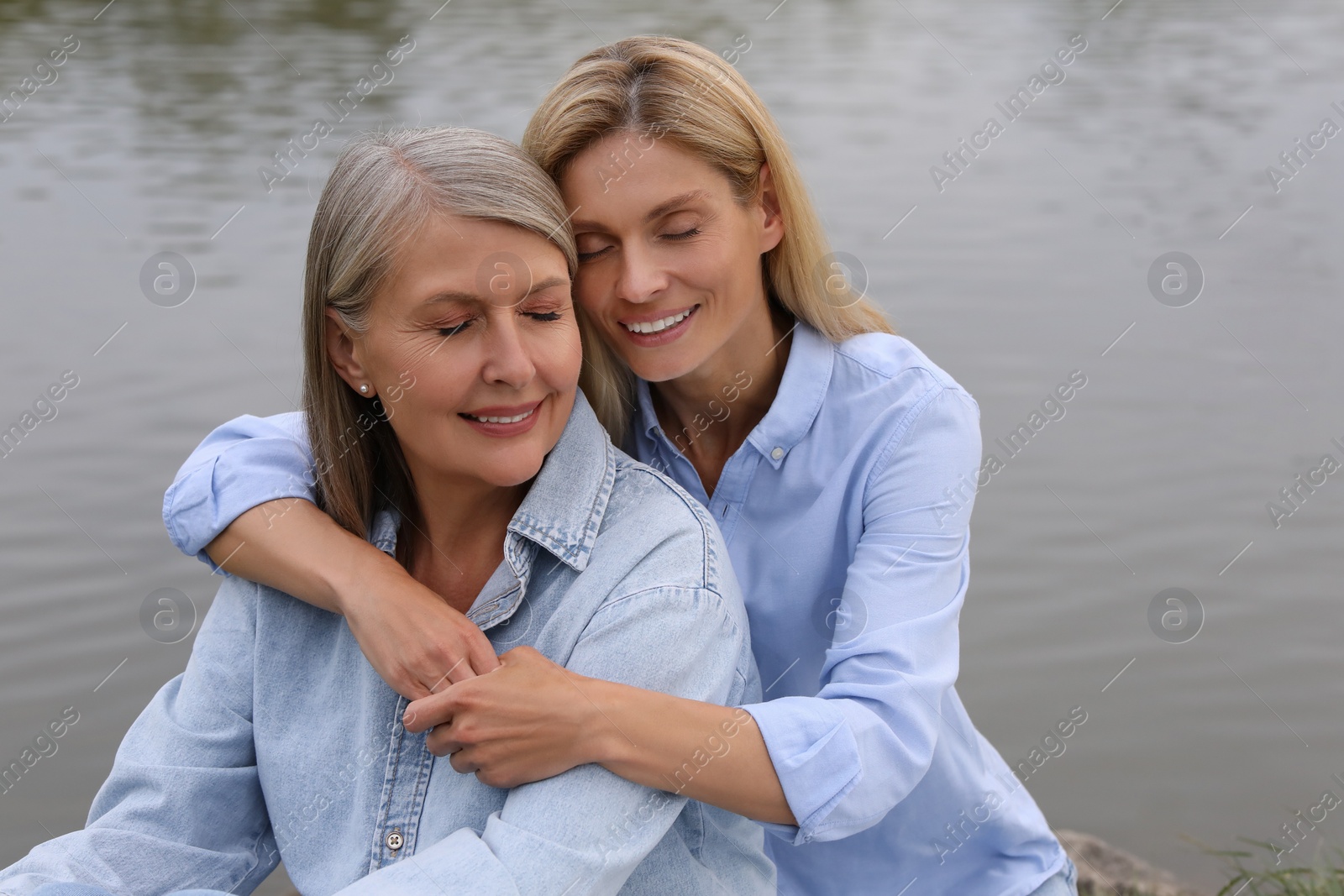 Photo of Happy mature mother and her daughter hugging near pond