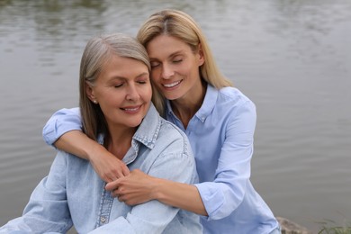 Photo of Happy mature mother and her daughter hugging near pond