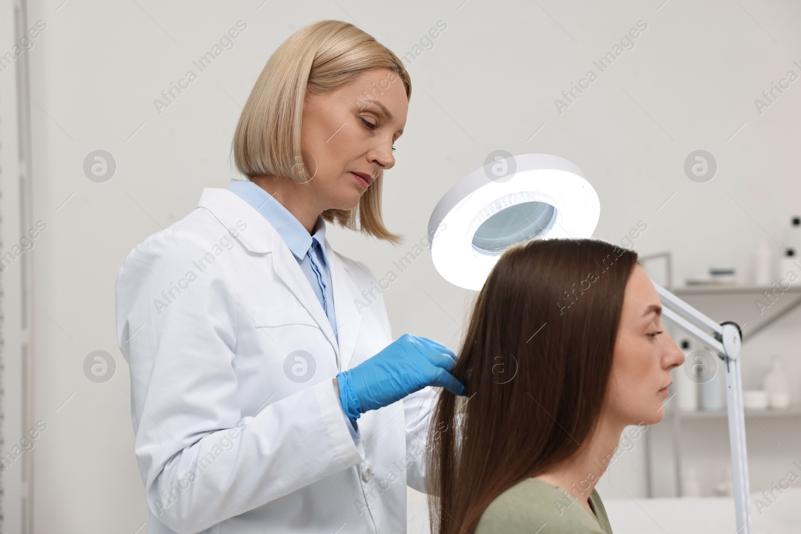 Photo of Trichologist examining patient`s hair under lamp in clinic