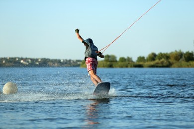 Photo of Teenage boy wakeboarding on river, back view. Extreme water sport