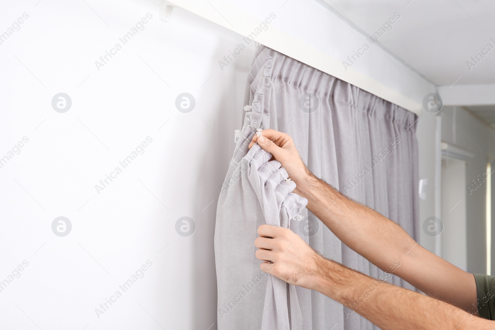 Photo of Man hanging window curtain indoors, closeup. Interior decor element