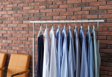 Photo of Wardrobe rack with men's clothes and chairs near brick wall