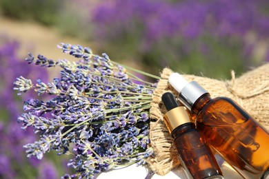 Bottles of essential oil and lavender flowers on white wooden table in field, closeup