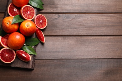 Photo of Ripe red oranges, green leaves and board on wooden table, top view. Space for text