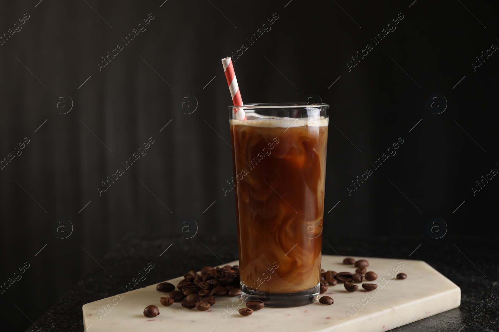 Photo of Refreshing iced coffee with milk in glass and beans on table against dark gray background, space for text