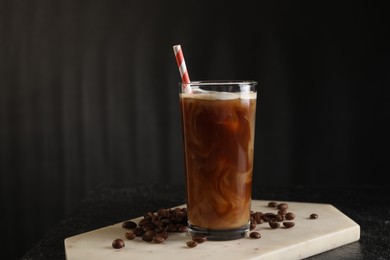 Photo of Refreshing iced coffee with milk in glass and beans on table against dark gray background, space for text