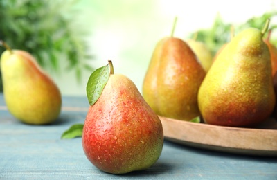 Photo of Ripe juicy pears on blue wooden table against blurred background