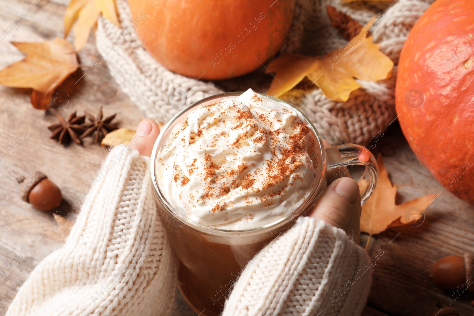 Photo of Woman holding cup with pumpkin spice latte on wooden table