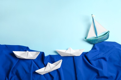 Photo of Handmade ships and fabric imitating waves on light blue background, flat lay. Space for text