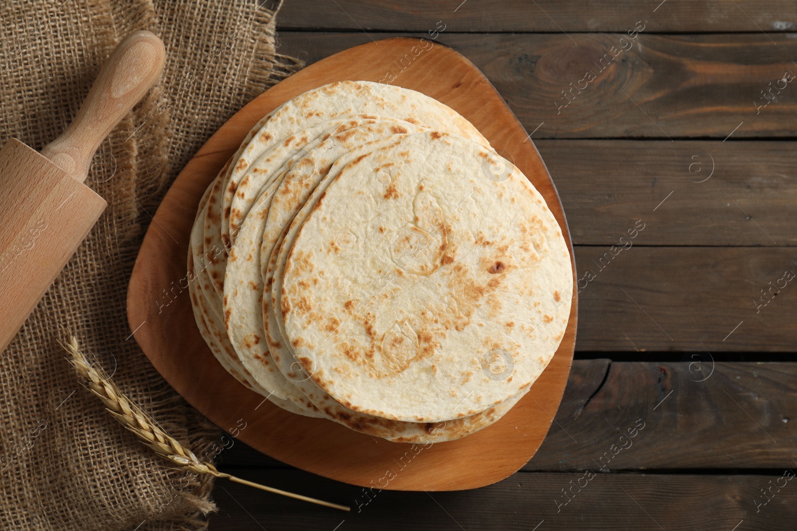 Photo of Many tasty homemade tortillas and rolling pin on wooden table, top view