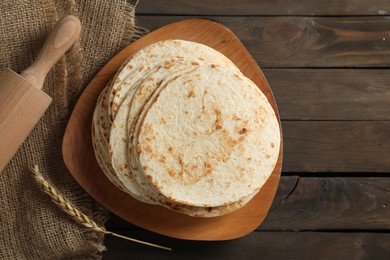 Many tasty homemade tortillas and rolling pin on wooden table, top view