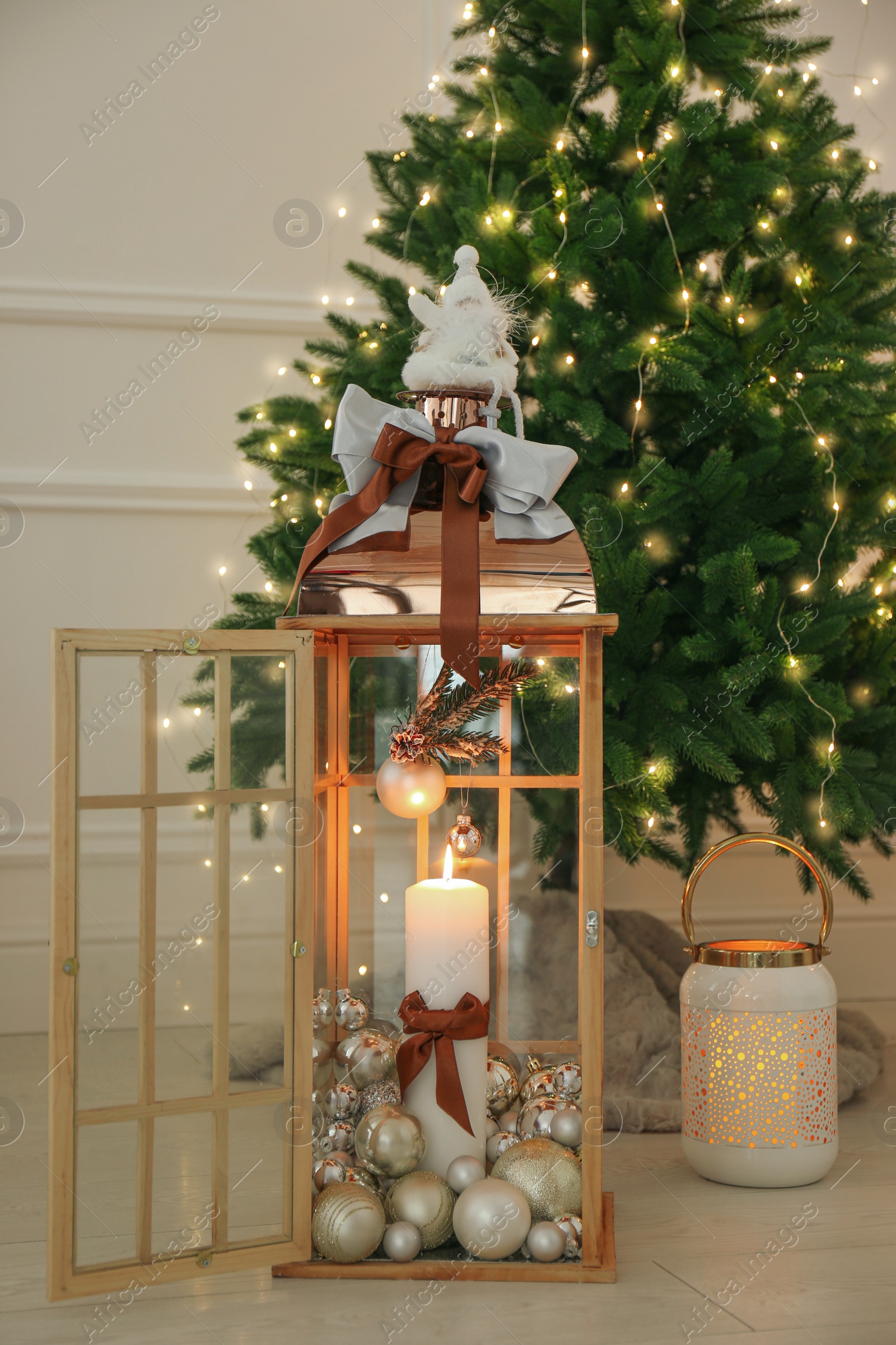 Photo of Wooden decorative lanterns with burning candles near Christmas tree indoors