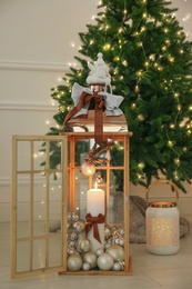 Photo of Wooden decorative lanterns with burning candles near Christmas tree indoors