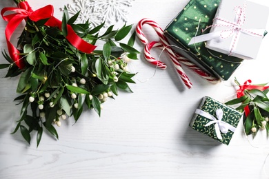 Photo of Mistletoe bunches, gift boxes and decorations on white wooden table, flat lay. Traditional Christmas decor