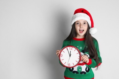 Photo of Girl in Santa hat with clock on white background, space for text. Christmas countdown