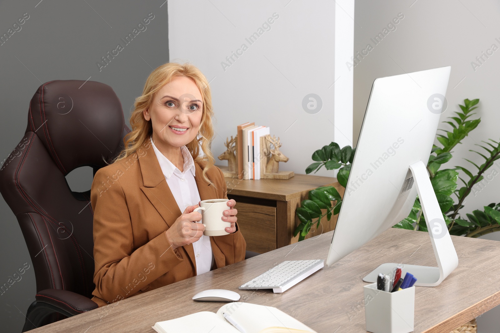 Photo of Lady boss with cup of drink near computer at desk in office. Successful businesswoman