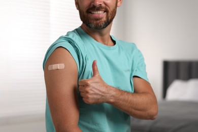 Photo of Man with sticking plaster on arm after vaccination showing thumbs up in bedroom, closeup