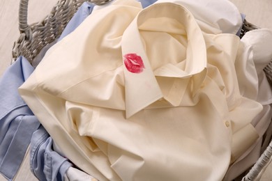 Photo of Men's shirt with lipstick kiss marks among other clothes in laundry basket indoors, closeup