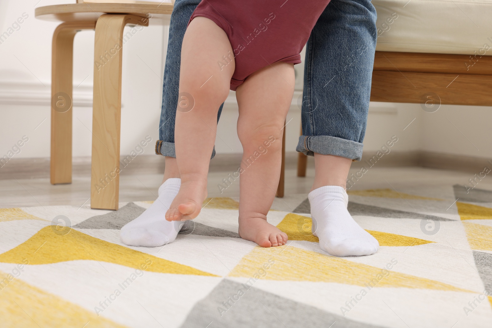 Photo of Mother supporting her baby son while he learning to walk on carpet at home, closeup