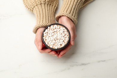 Photo of Woman with cup of tasty hot chocolate and marshmallows at white marble table, top view