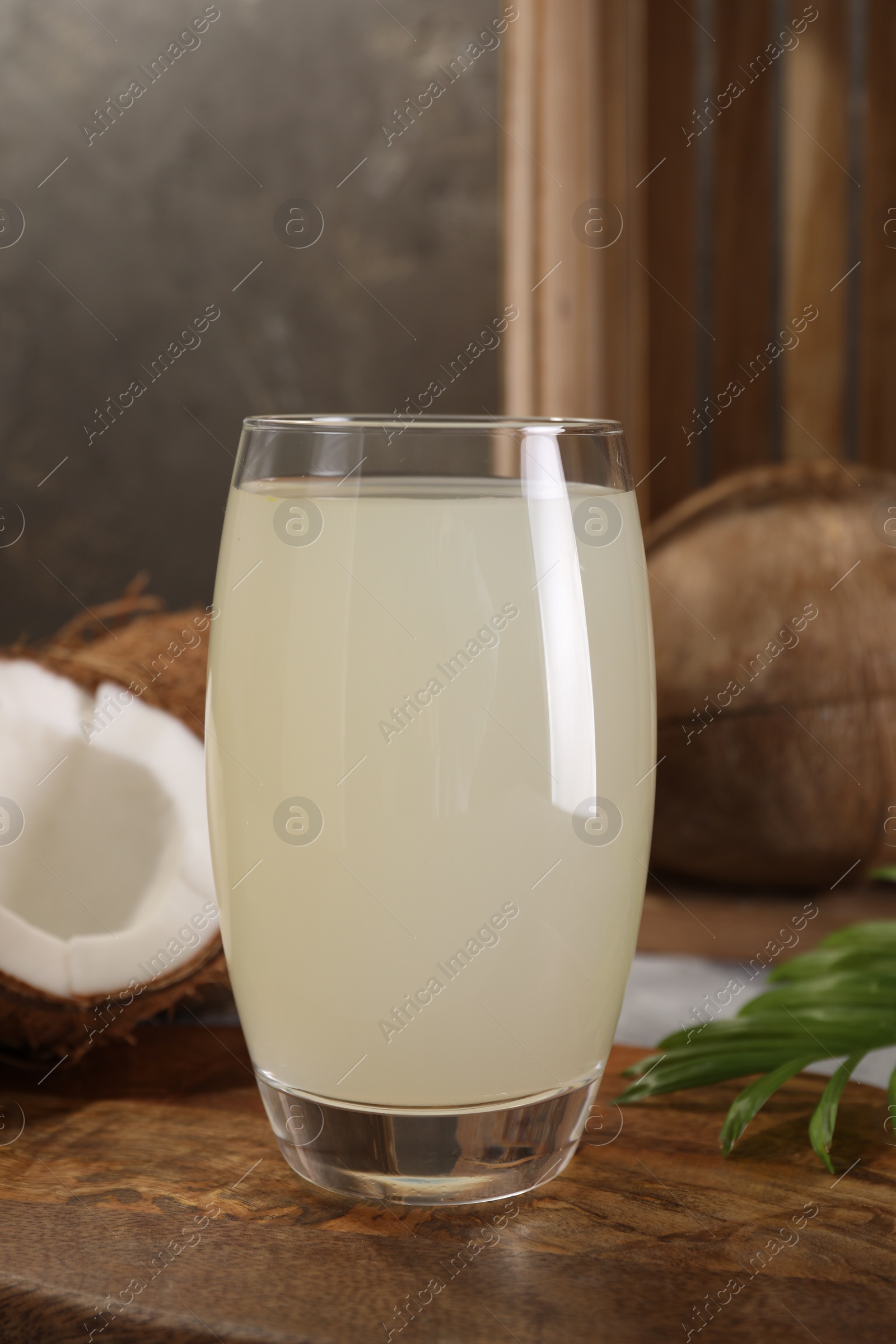 Photo of Glass of coconut water, palm leaf and nuts on grey table