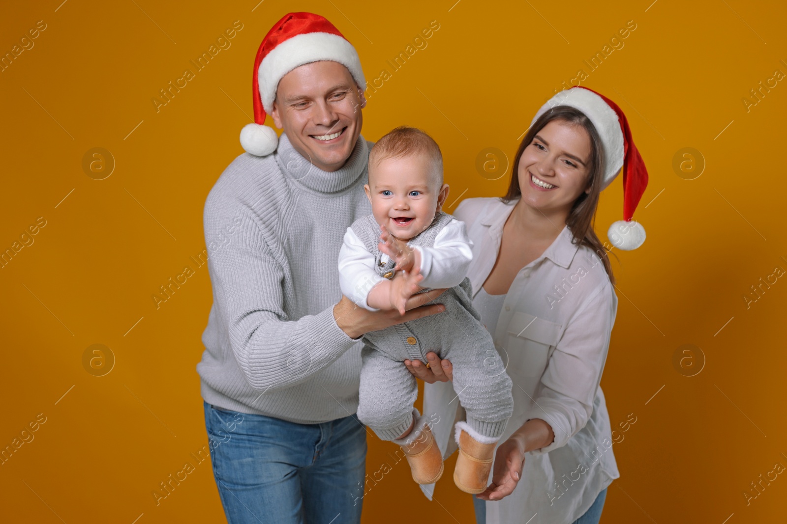 Photo of Happy couple with cute baby wearing Santa hats on yellow background. Christmas season