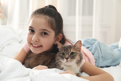 Cute little girl with cat lying on bed at home. First pet