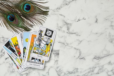 Tarot cards and peacock feathers on white marble table, flat lay. Space for text