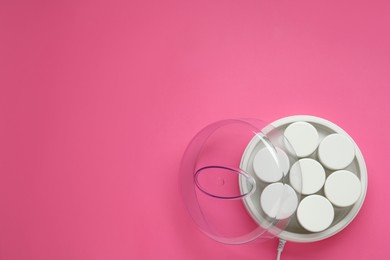 Modern yogurt maker with jars on pink background, top view. Space for text