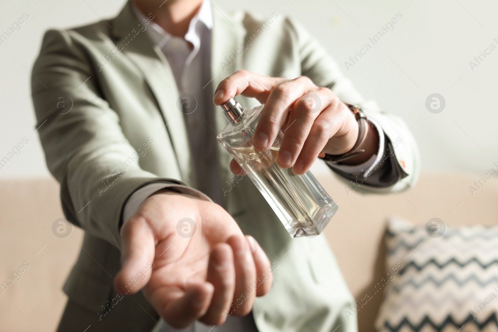 Photo of Man applying perfume on wrist indoors, closeup