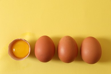 Photo of Cracked and whole chicken eggs on yellow background, flat lay. Space for text