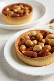 Photo of Tartlets with caramelized nuts on white wooden table, closeup. Tasty dessert