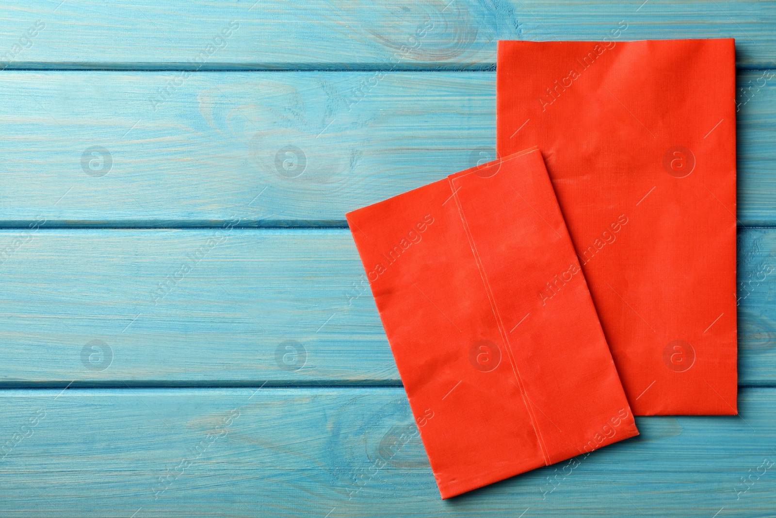 Photo of Red reusable beeswax food wraps on light blue wooden table, top view. Space for text