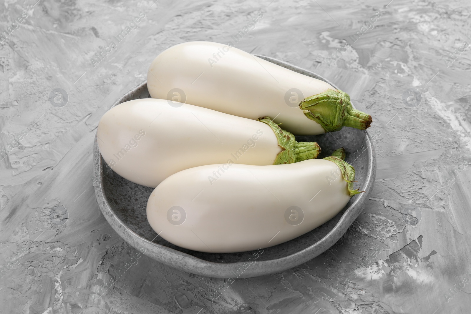 Photo of Fresh white eggplants in bowl on grey textured table