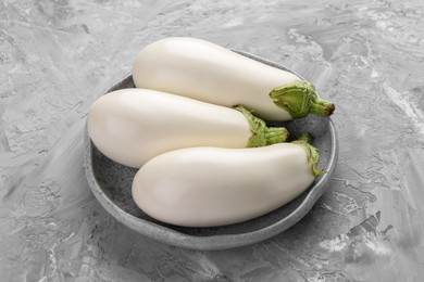 Photo of Fresh white eggplants in bowl on grey textured table