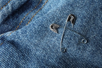Photo of Metal safety pins on denim fabric, closeup