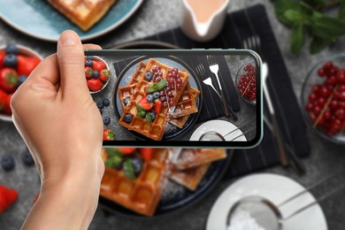 Image of Woman taking picture of delicious Belgian waffles with berries served on grey table, top view