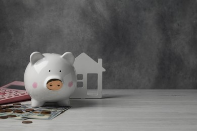 Photo of Piggy bank, house model, calculator and money on white wooden table. Space for text