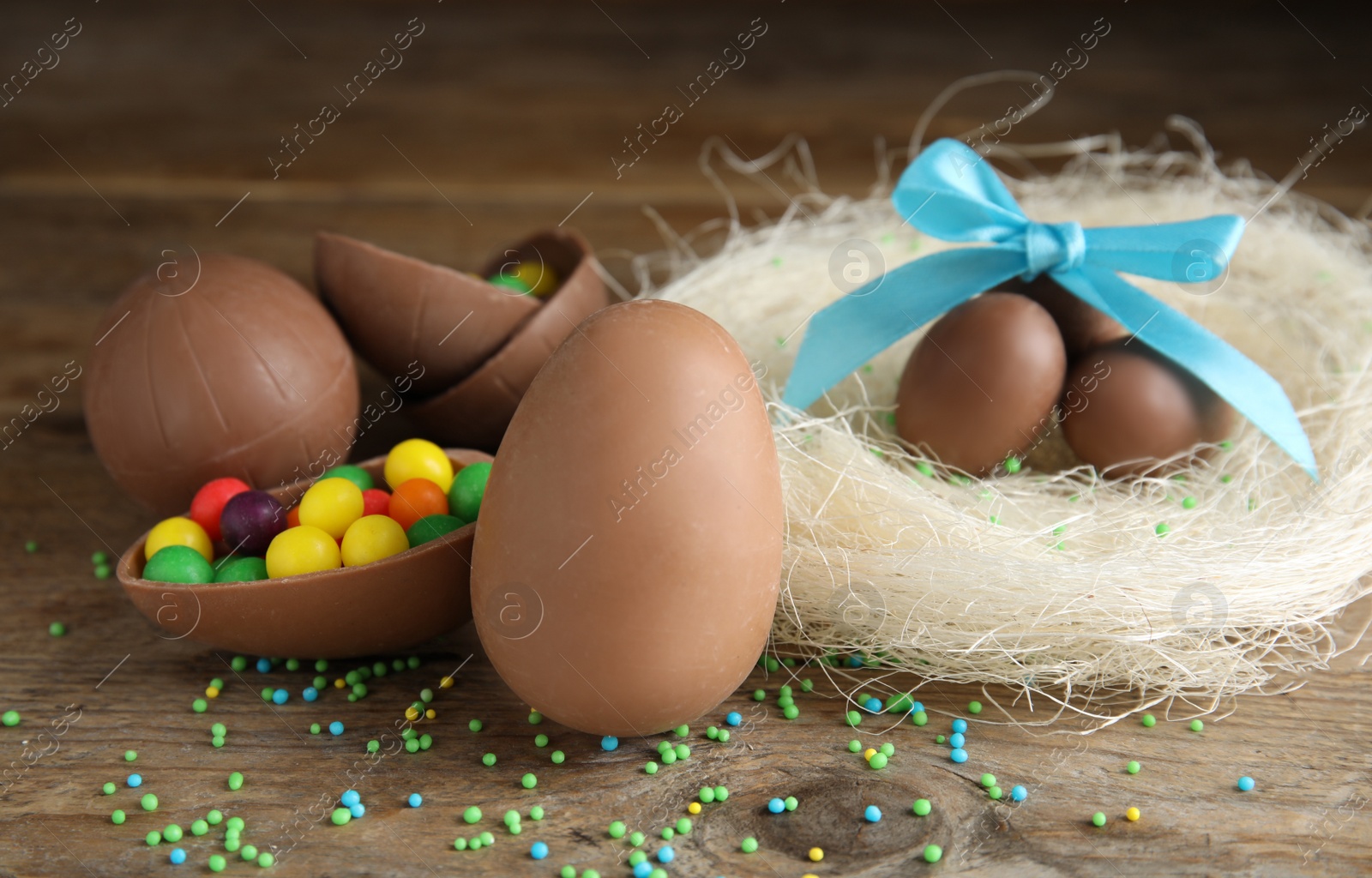 Photo of Composition with tasty chocolate eggs, colorful candies and decorative nest on wooden table