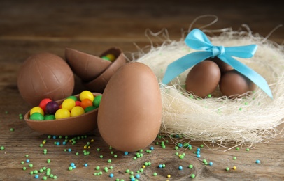 Photo of Composition with tasty chocolate eggs, colorful candies and decorative nest on wooden table