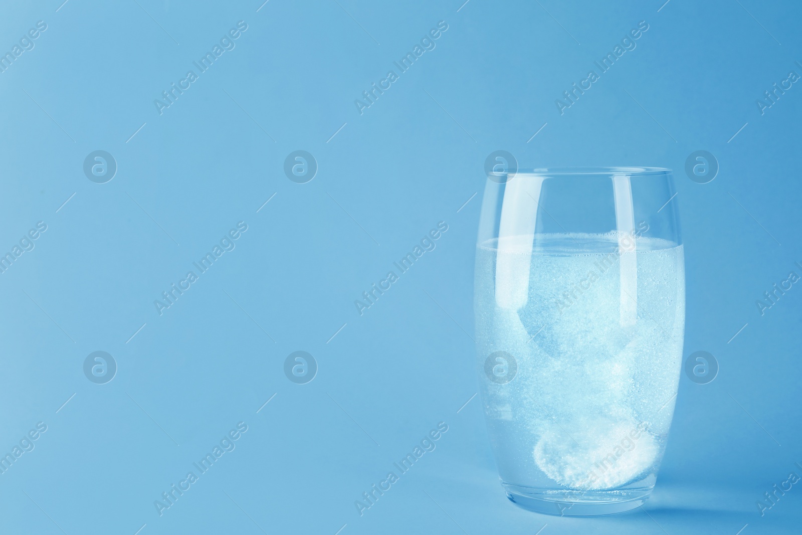 Photo of Glass of water with effervescent tablet on light grey background, space for text