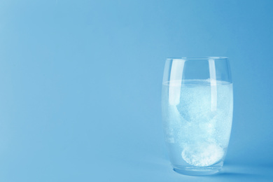 Photo of Glass of water with effervescent tablet on light grey background, space for text