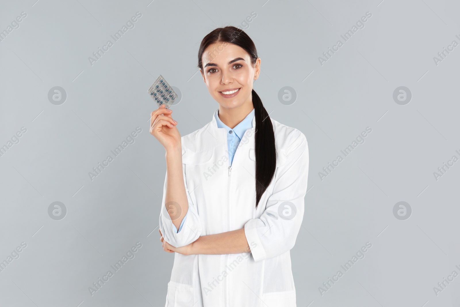 Photo of Professional pharmacist with pills on light grey background