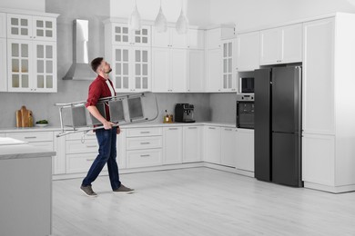 Young man carrying metal stepladder in kitchen, space for text