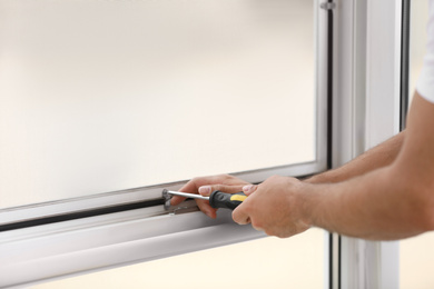 Construction worker repairing plastic window with screwdriver indoors, closeup